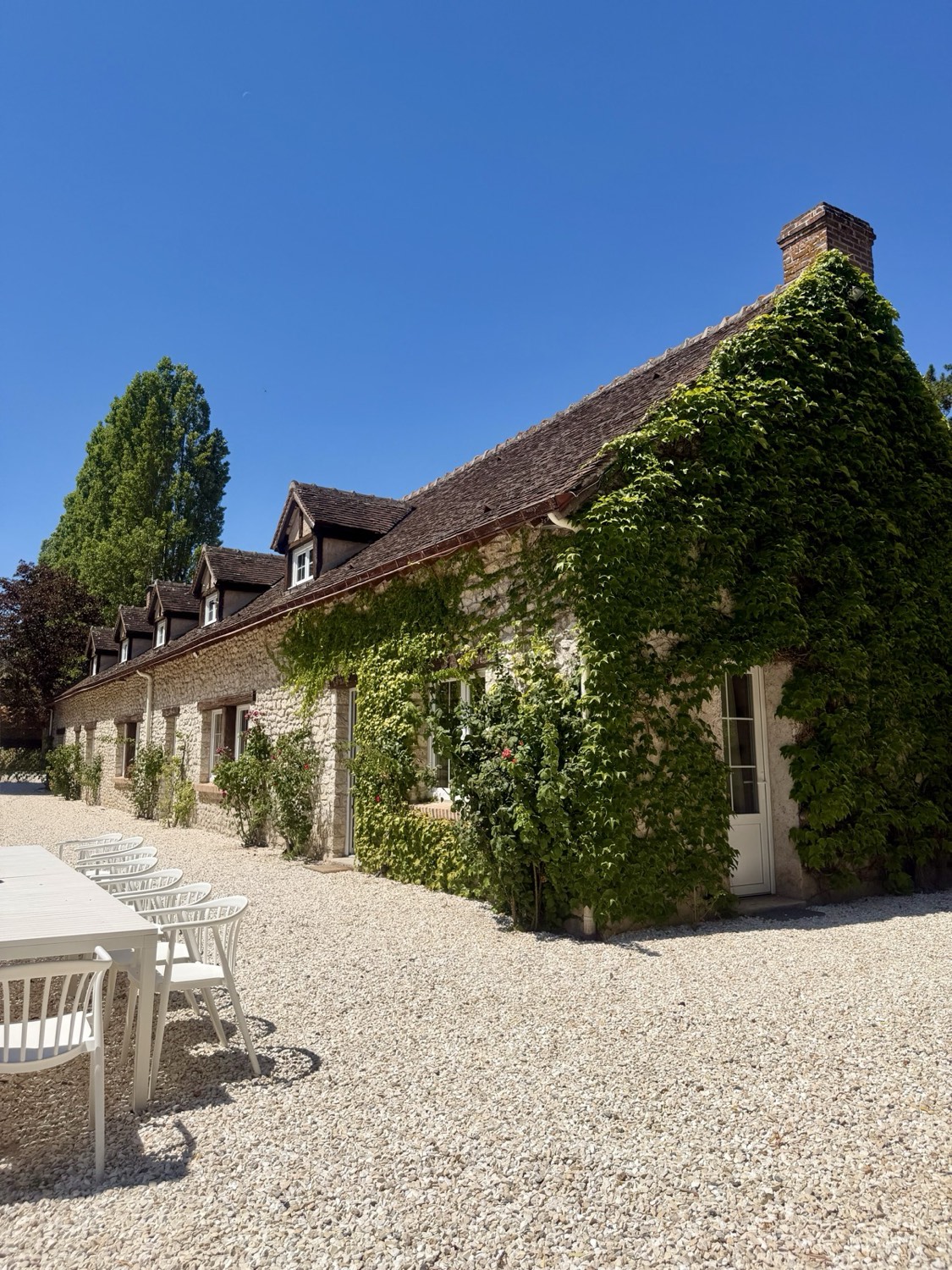 La façade en pierre couverte de vigne et sa cour gravillonnée
